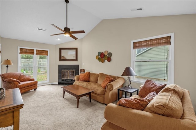 carpeted living area with a ceiling fan, a tile fireplace, visible vents, and vaulted ceiling