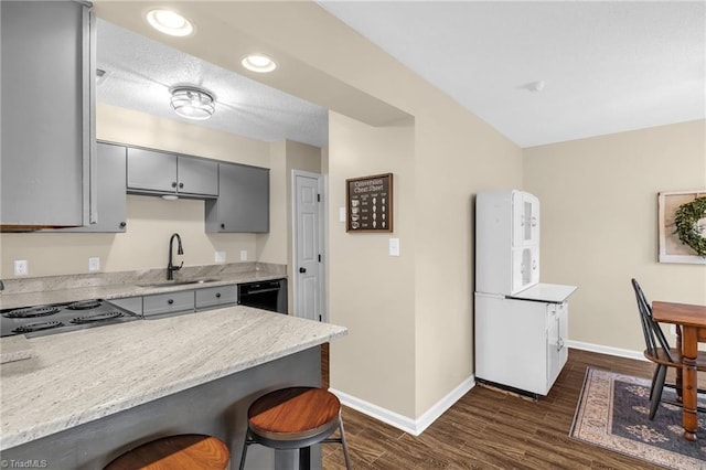 kitchen featuring dishwasher, dark wood-style flooring, gray cabinetry, a kitchen bar, and a sink