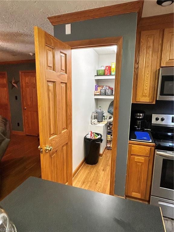 kitchen with brown cabinets, dark countertops, appliances with stainless steel finishes, light wood-style flooring, and baseboards
