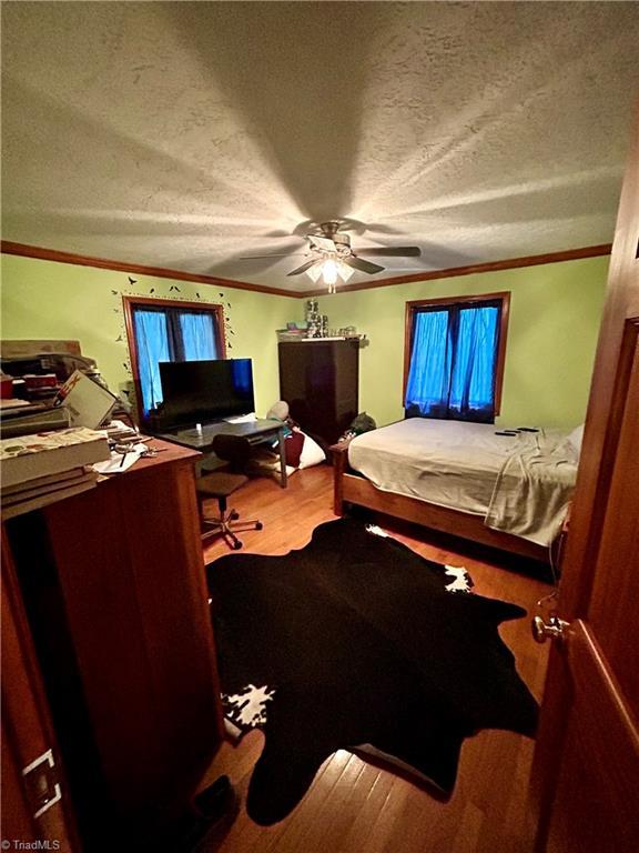 bedroom with ornamental molding, a textured ceiling, a ceiling fan, and wood finished floors