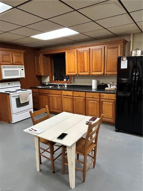kitchen featuring white appliances, dark countertops, brown cabinetry, and a paneled ceiling
