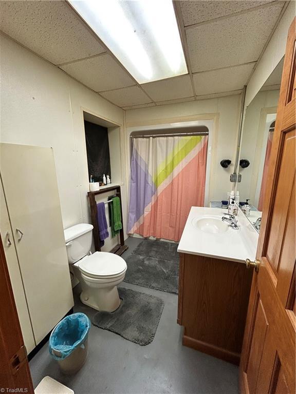 bathroom with finished concrete floors, a paneled ceiling, toilet, and vanity