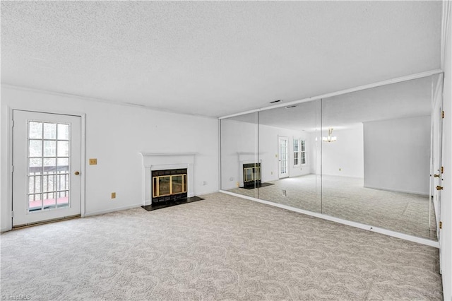 unfurnished living room with baseboards, a fireplace with flush hearth, a textured ceiling, carpet floors, and a notable chandelier