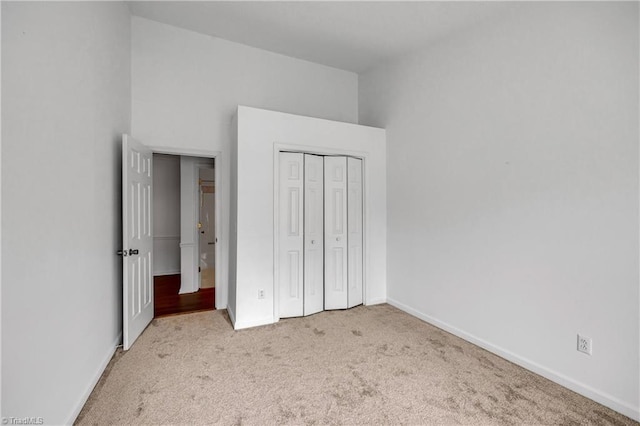 unfurnished bedroom featuring high vaulted ceiling, a closet, carpet flooring, and baseboards