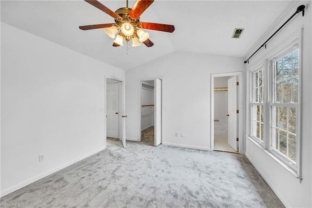 unfurnished bedroom with carpet, a walk in closet, lofted ceiling, connected bathroom, and baseboards