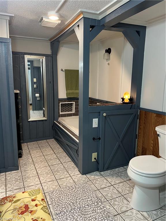 bathroom featuring wood walls, a bath, tile patterned floors, toilet, and a textured ceiling