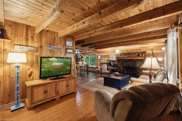 living room featuring beam ceiling, a stone fireplace, wood-type flooring, and wood walls