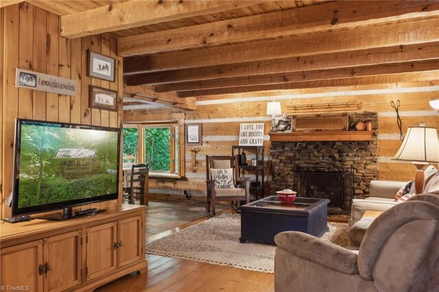 living room with beamed ceiling, wooden walls, a stone fireplace, light wood-type flooring, and wooden ceiling