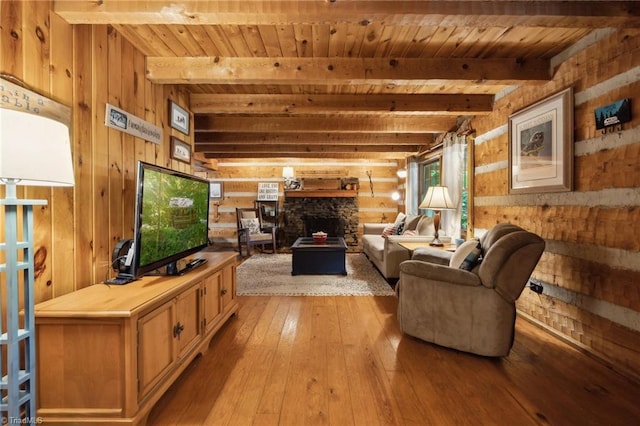 living room featuring beam ceiling, wooden walls, light hardwood / wood-style floors, wooden ceiling, and a stone fireplace