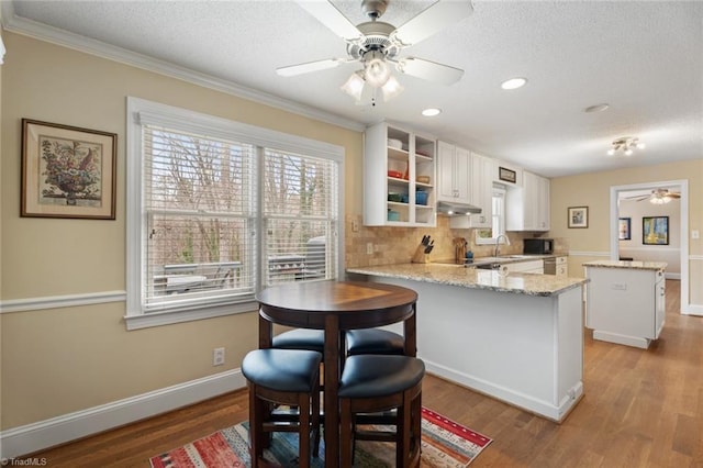 kitchen featuring white cabinets, a kitchen island, wood finished floors, a peninsula, and under cabinet range hood