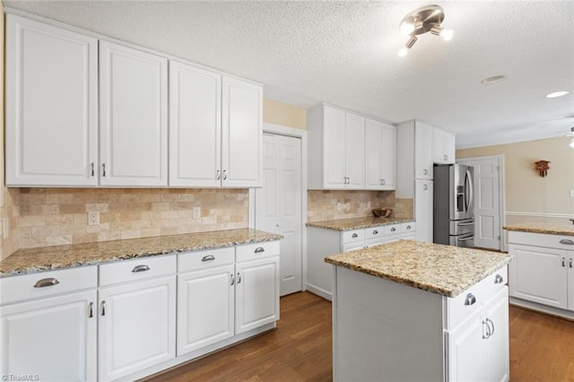 kitchen with dark wood-style floors, stainless steel fridge, a center island, and white cabinets