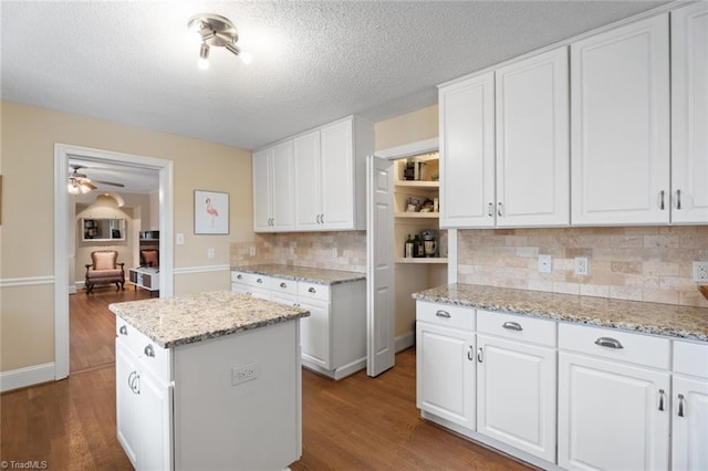 kitchen featuring light stone counters, tasteful backsplash, white cabinetry, a kitchen island, and wood finished floors