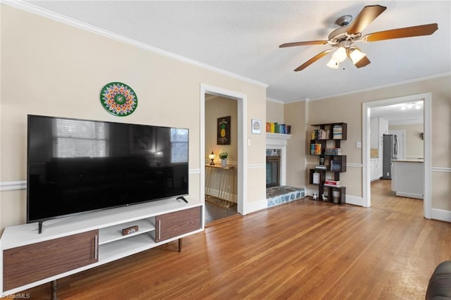 unfurnished living room with crown molding, ceiling fan, wood finished floors, and a glass covered fireplace