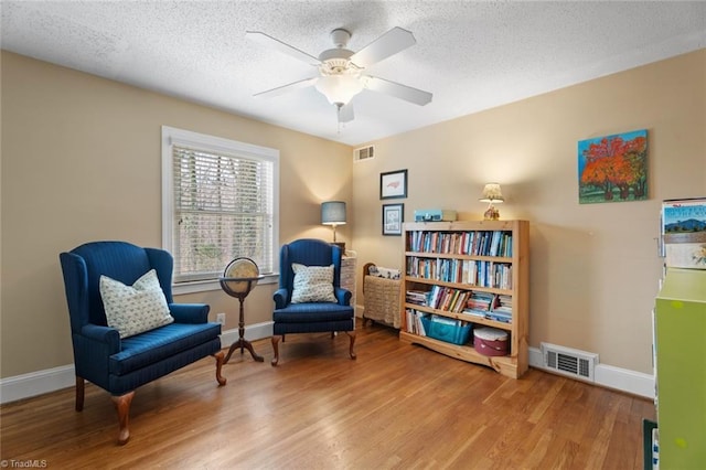 living area with a textured ceiling, wood finished floors, visible vents, and baseboards