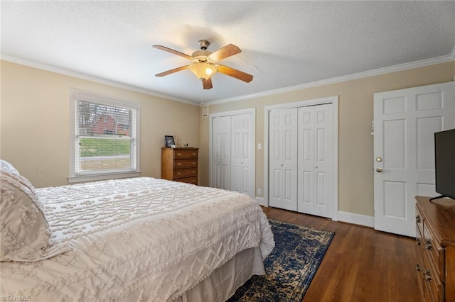 bedroom with a textured ceiling, wood finished floors, baseboards, two closets, and crown molding