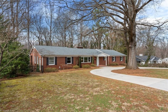 single story home with driveway, brick siding, a chimney, and a front yard