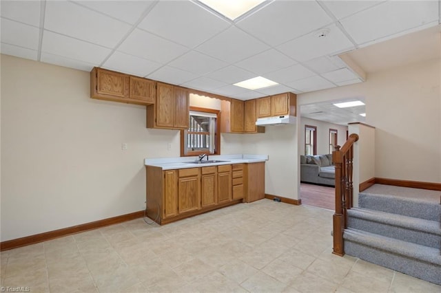 kitchen featuring a drop ceiling, under cabinet range hood, a sink, baseboards, and light countertops