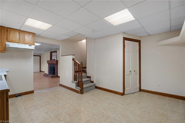 spare room with a paneled ceiling, a brick fireplace, baseboards, and stairway