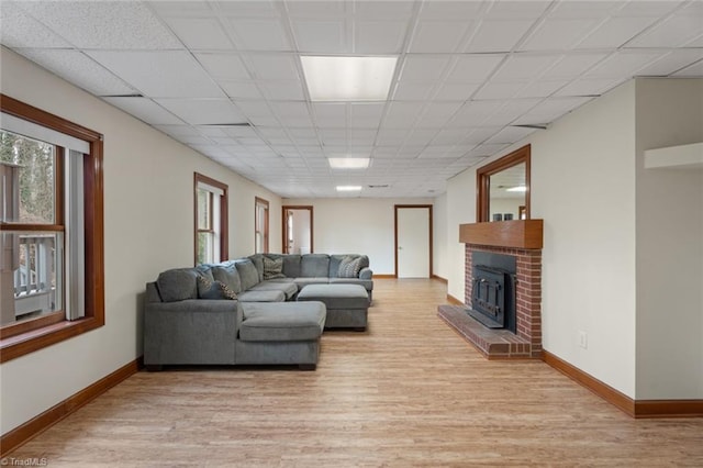 living area featuring baseboards, a drop ceiling, and light wood finished floors