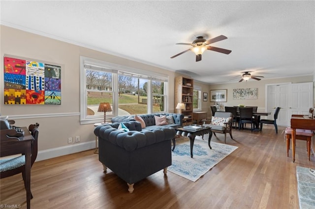 living room with light wood-type flooring, crown molding, a textured ceiling, and baseboards