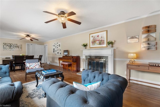 living area featuring crown molding, a fireplace, ceiling fan, wood finished floors, and baseboards