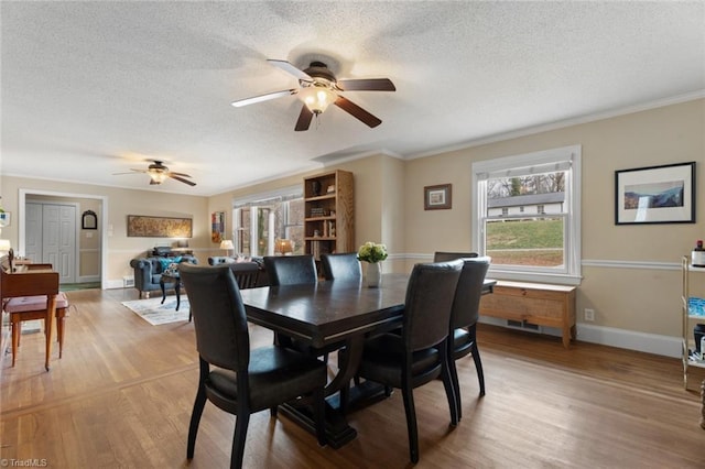 dining area featuring light wood-style floors, baseboards, ornamental molding, and a textured ceiling