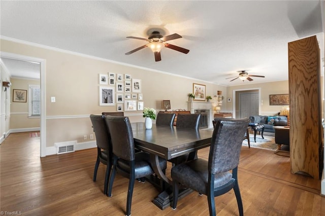 dining space with a fireplace, visible vents, ornamental molding, a textured ceiling, and wood finished floors