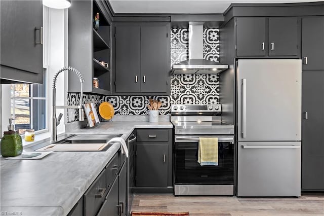 kitchen with light wood finished floors, open shelves, a sink, stainless steel appliances, and wall chimney exhaust hood