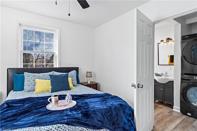 bedroom featuring a sink, wood finished floors, a ceiling fan, and stacked washing maching and dryer