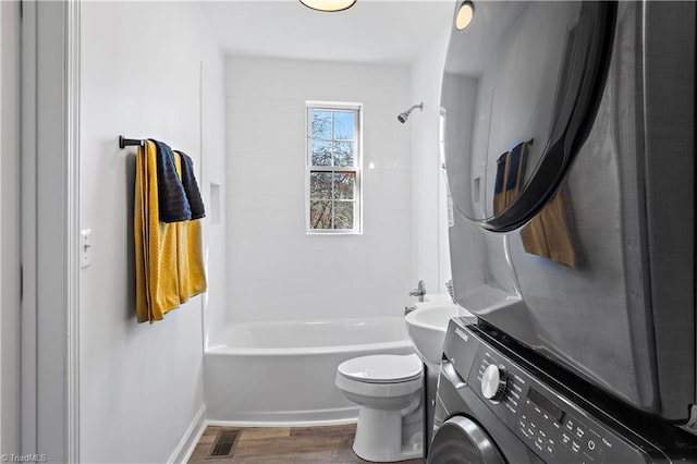 bathroom with toilet, vanity, stacked washer and dryer, wood finished floors, and washtub / shower combination