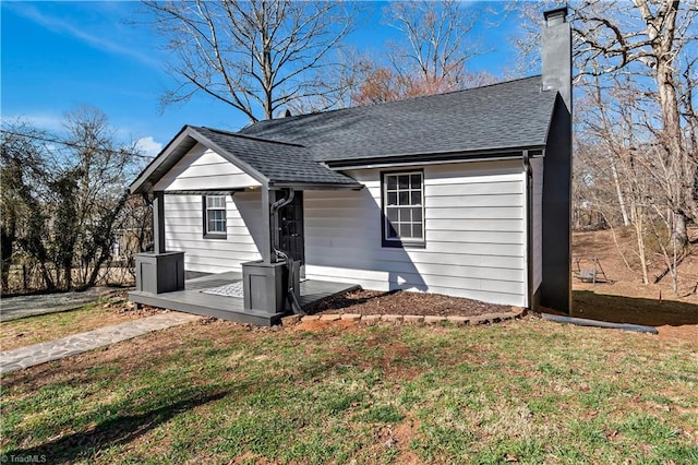 view of front of house featuring a chimney, a front lawn, and roof with shingles