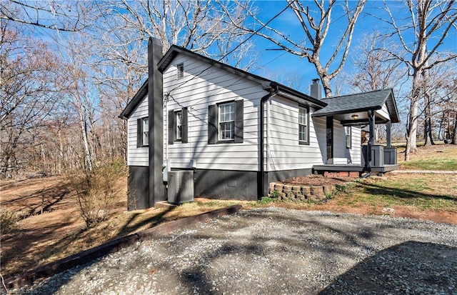 view of side of property with covered porch, a chimney, and roof with shingles