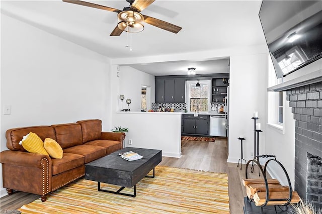 living area featuring a brick fireplace, a ceiling fan, and light wood-style floors