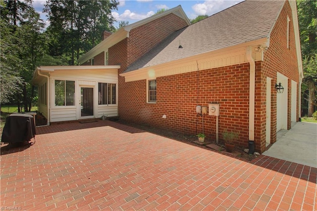 rear view of property with a garage, a patio area, a shingled roof, and brick siding