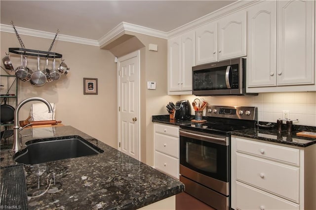 kitchen with white cabinets, crown molding, appliances with stainless steel finishes, sink, and dark stone counters