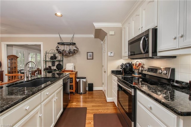 kitchen featuring light wood finished floors, ornamental molding, a sink, stainless steel appliances, and backsplash