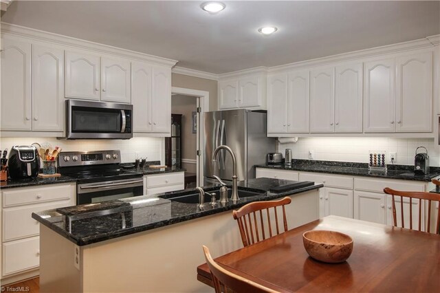 kitchen with an island with sink, stainless steel appliances, sink, ornamental molding, and decorative backsplash