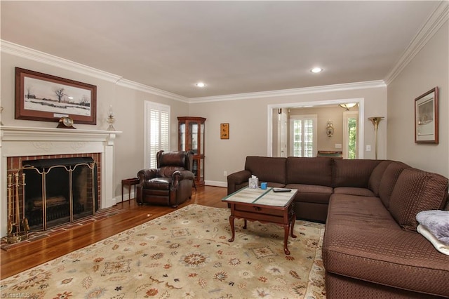 living room featuring a wealth of natural light, crown molding, wood-type flooring, and a brick fireplace