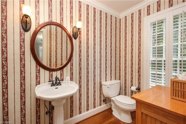 bathroom featuring wallpapered walls, baseboards, toilet, wood finished floors, and crown molding