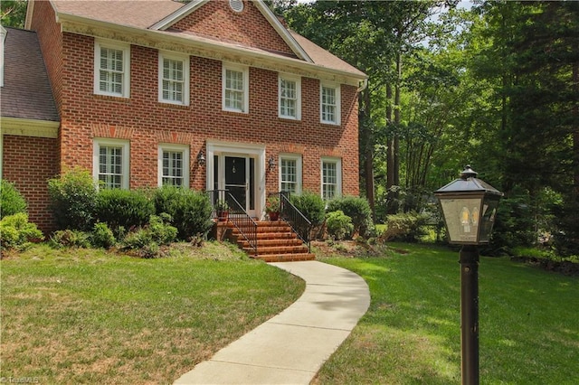 colonial-style house featuring roof with shingles, brick siding, and a front lawn