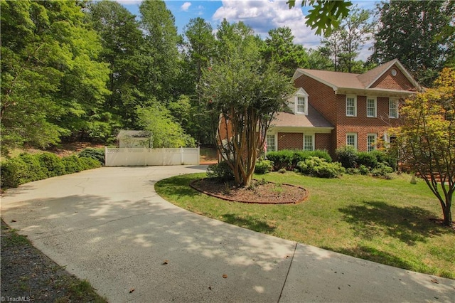 view of front facade featuring concrete driveway, a front lawn, fence, and brick siding