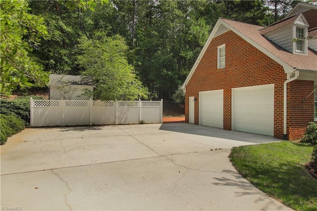 view of home's exterior featuring brick siding, roof with shingles, concrete driveway, fence, and a garage