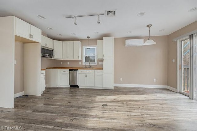 kitchen with sink, hardwood / wood-style flooring, appliances with stainless steel finishes, pendant lighting, and white cabinets