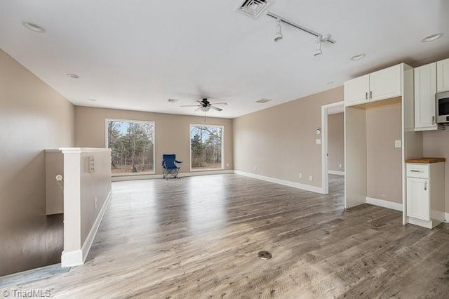 unfurnished living room featuring track lighting, ceiling fan, and light hardwood / wood-style flooring