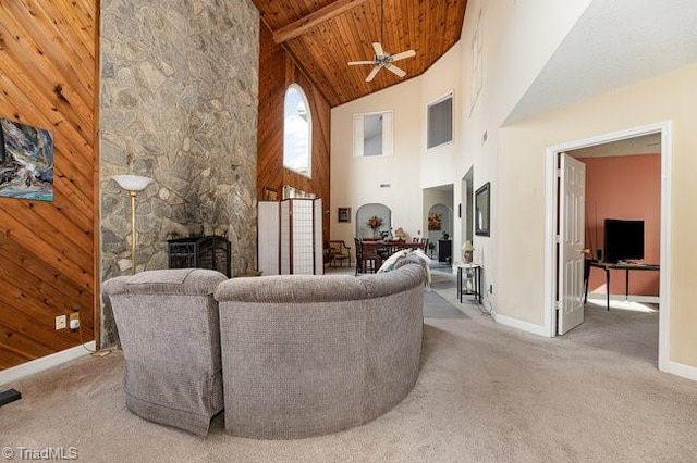 carpeted living room with a stone fireplace, high vaulted ceiling, wooden walls, ceiling fan, and wooden ceiling