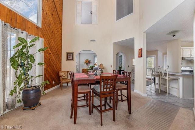 carpeted dining space with a towering ceiling and wood walls