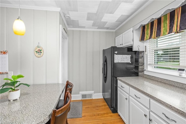 kitchen featuring black refrigerator, hanging light fixtures, light wood-type flooring, ornamental molding, and white cabinetry