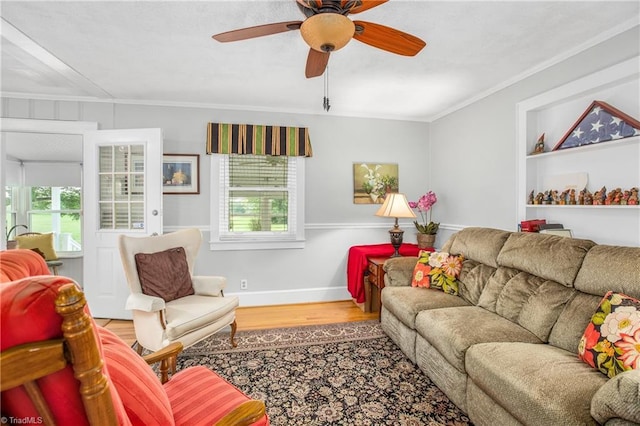 living room with built in shelves, ceiling fan, ornamental molding, and hardwood / wood-style floors