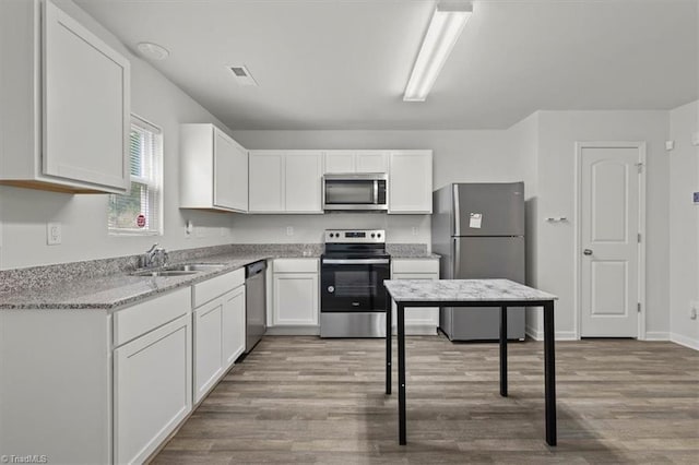 kitchen featuring a sink, stainless steel appliances, light stone counters, white cabinetry, and wood finished floors