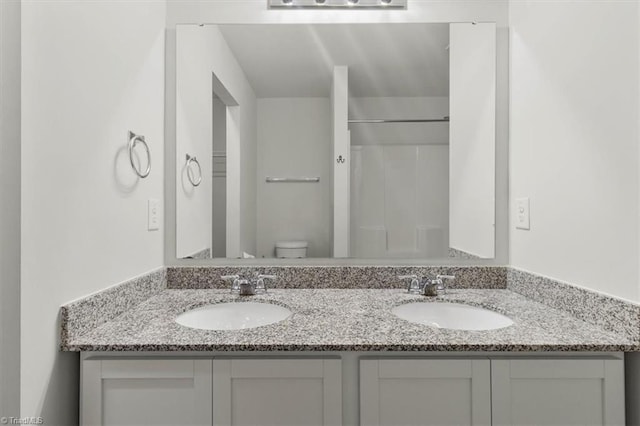bathroom featuring toilet, double vanity, a sink, and a shower